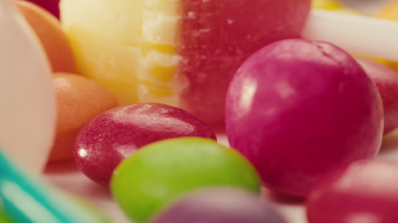 Colorful dragee candies, lollipops, bonbons on white background, move in circle, side view close-up. Summer bright texture studio shot for store, supermarket. Mix of children's sweets made of sugar.