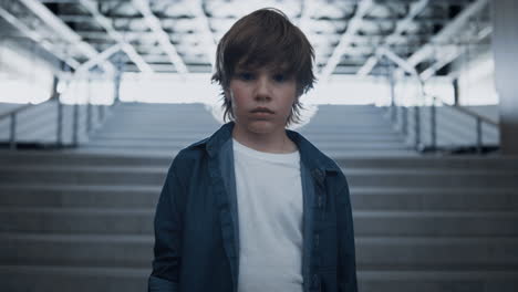 depressed school boy standing alone at empty staircase close up. fearful eyes