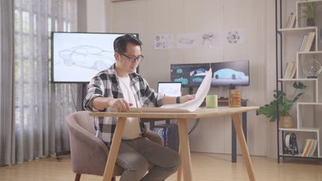 satisfied asian male holding and looking at car design sketch then shaking his head while working on table in the studio with tv and computers display 3d electric car model