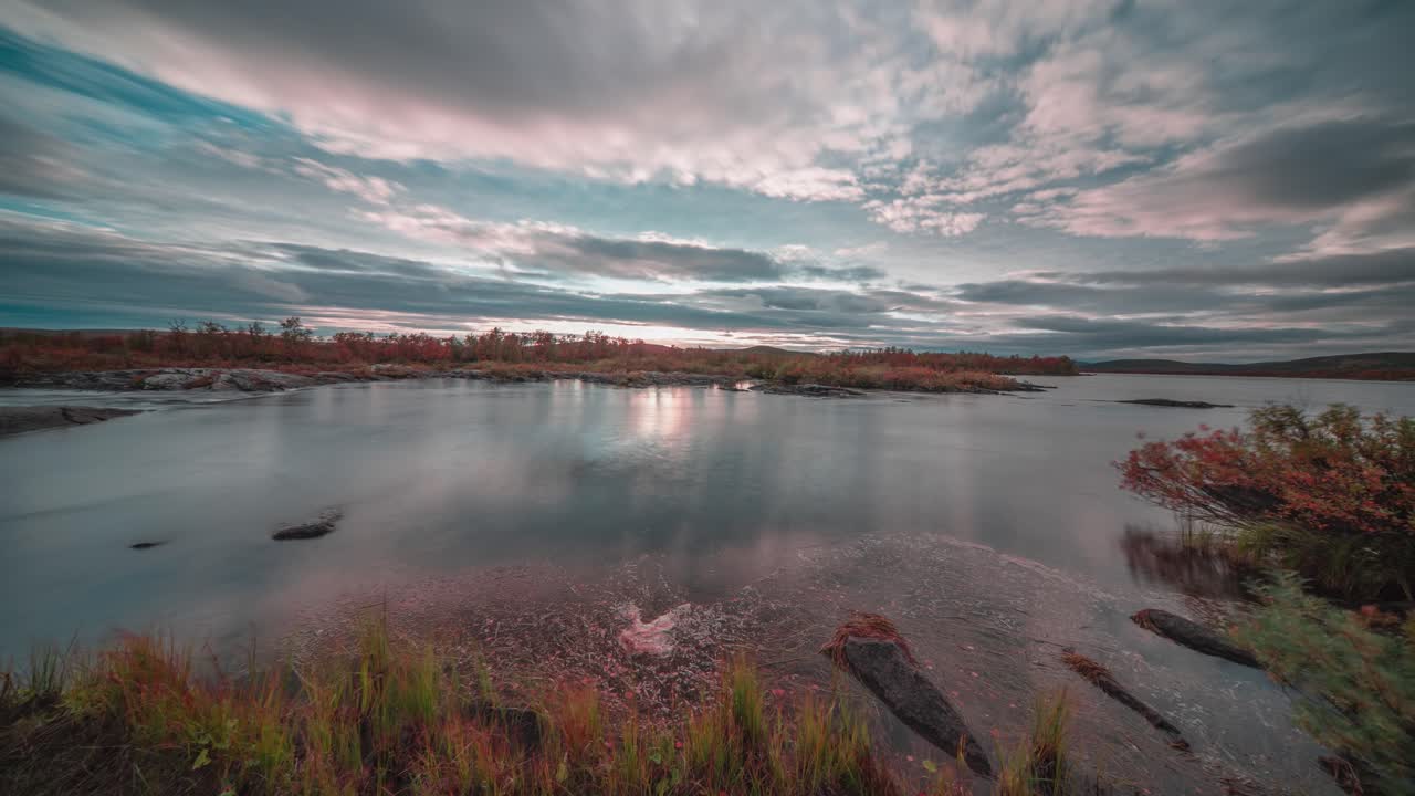 las nubes tormentosas se mueven rápidamente en los cielos del atardecer mientras la oscuridad cae sobre el río tranquilo y las orillas cubiertas de hierba.