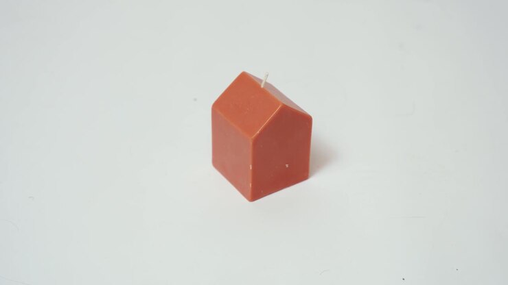 Small Orange Wax House Shaped Fire Scented Candle Against a White Paper Backdrop