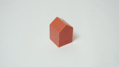 Small-Orange-Wax-House-Shaped-Fire-Scented-Candle-Against-a-White-Paper-Backdrop