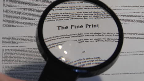 a magnifying glass passes over a paper to reveal the words the fine print