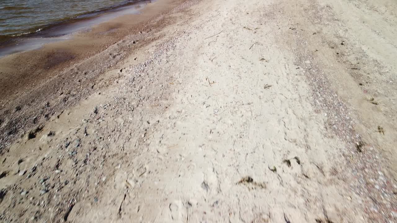 화창한 봄날 하얀 모래가 있는 해변에 파도가 부딪히는 공중 저고도, 발트해, 파페 해변, 라트비아, 광각 드론 샷이 카메라를 위로 기울입니다.