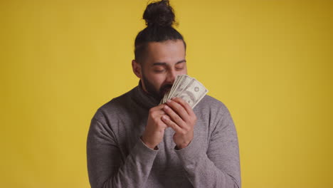 studio shot of excited young man celebrating winning cash prize holding handful of 100 dollar bills against yellow background