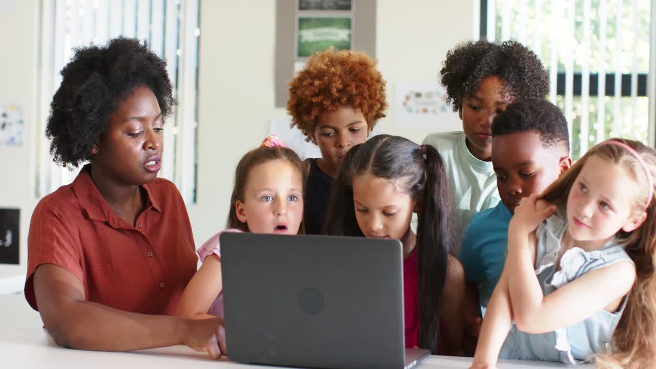 African American teacher guiding youths, placing hand on laptop and sparking curiosity in classroom