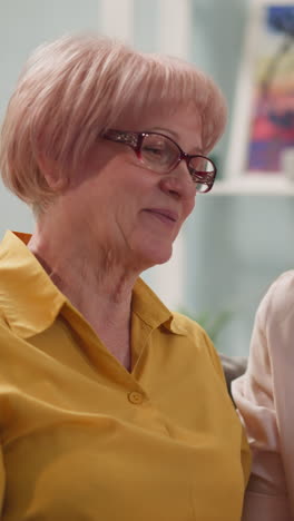 elderly mother consults with an adult daughter, woman tries to understand how to work remotely with laptop, smiles, in glasses, in room, next to green plant in pot