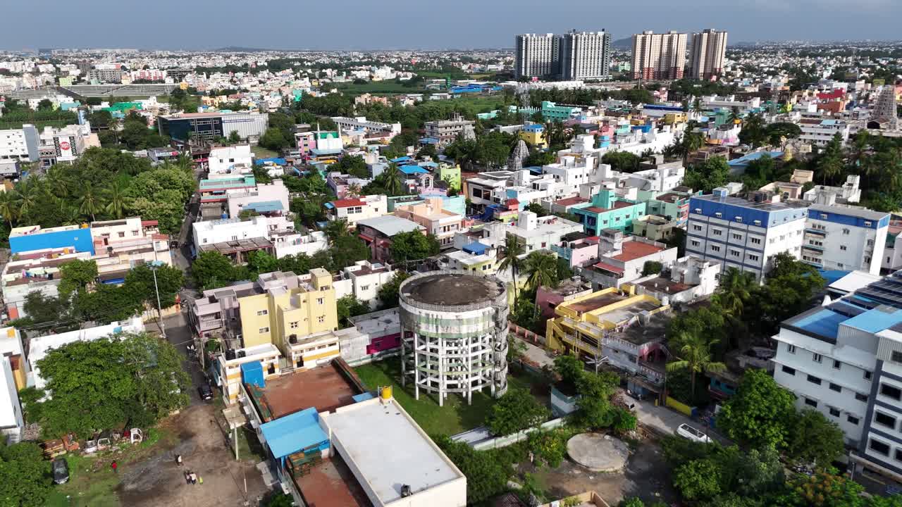 A high-angle aerial shot of a large, circular water tank in the center of a bustling residential neighborhood in India. captures colorful houses, rooftops, and green trees typical urban infrastructure