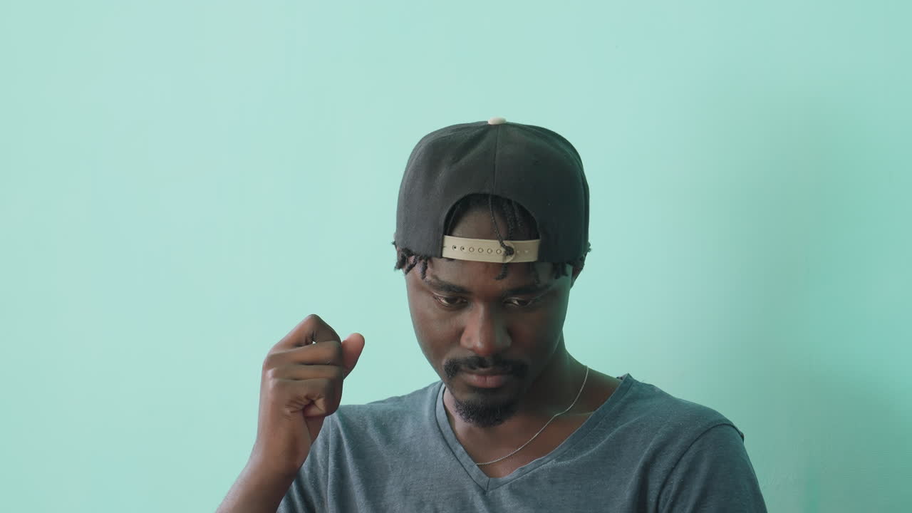 Close up of young man seated indoors, legs crossed, deeply focused on reading hardcover book while gently touching face, wearing casual grey shirt