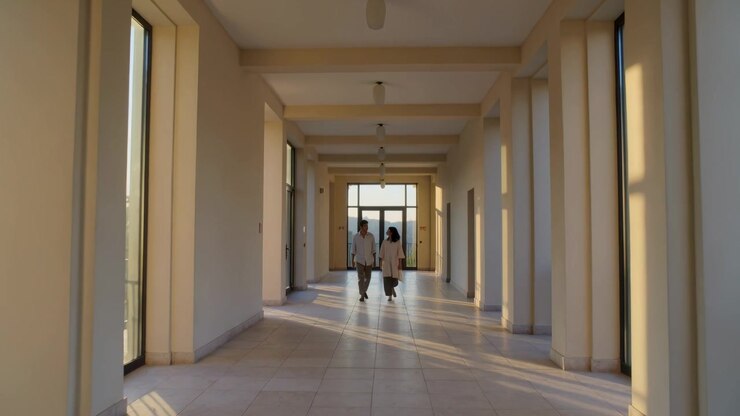Walking companions on cue moving to pass camera in hall with columns, light shirt, dark skirt