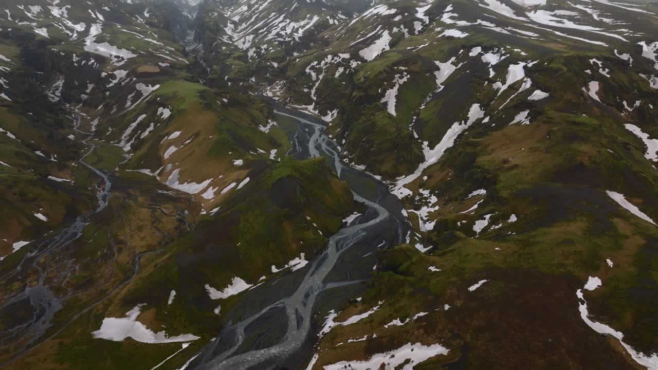vista aérea del paisaje sobre un río que fluye a través de montañas cubiertas de nieve derretida, en un día nublado y brumoso, en islandia
