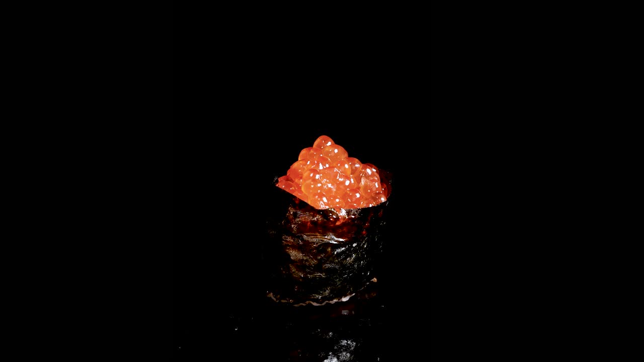 Salmon roe sushi rotates smoothly under dramatic lighting, highlighting glossy orange fish eggs and seaweed wrap against a seamless black background in a studio setting