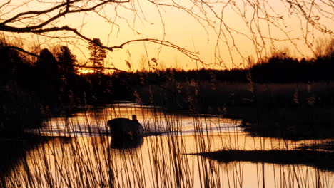 Summer-nights-in-Finland,-Silhouette-person-driving-boat-on-calm-river-at-golden-hour-sunset