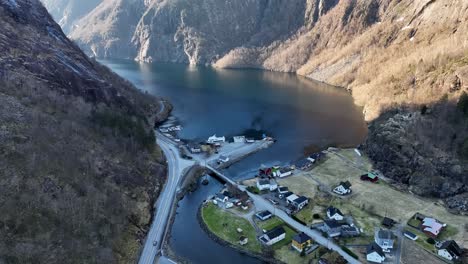 Mowi industrial building with river flowing toward Akrafjorden, surrounded by mountains. Aerial tilt up in winter with no snow