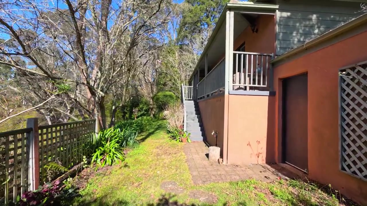 Camera moves through a garden archway past a wooden lattice toward an outdoor staircase.