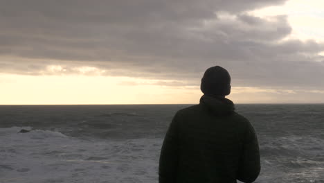 depressed man overlooks stormy sea at sunset