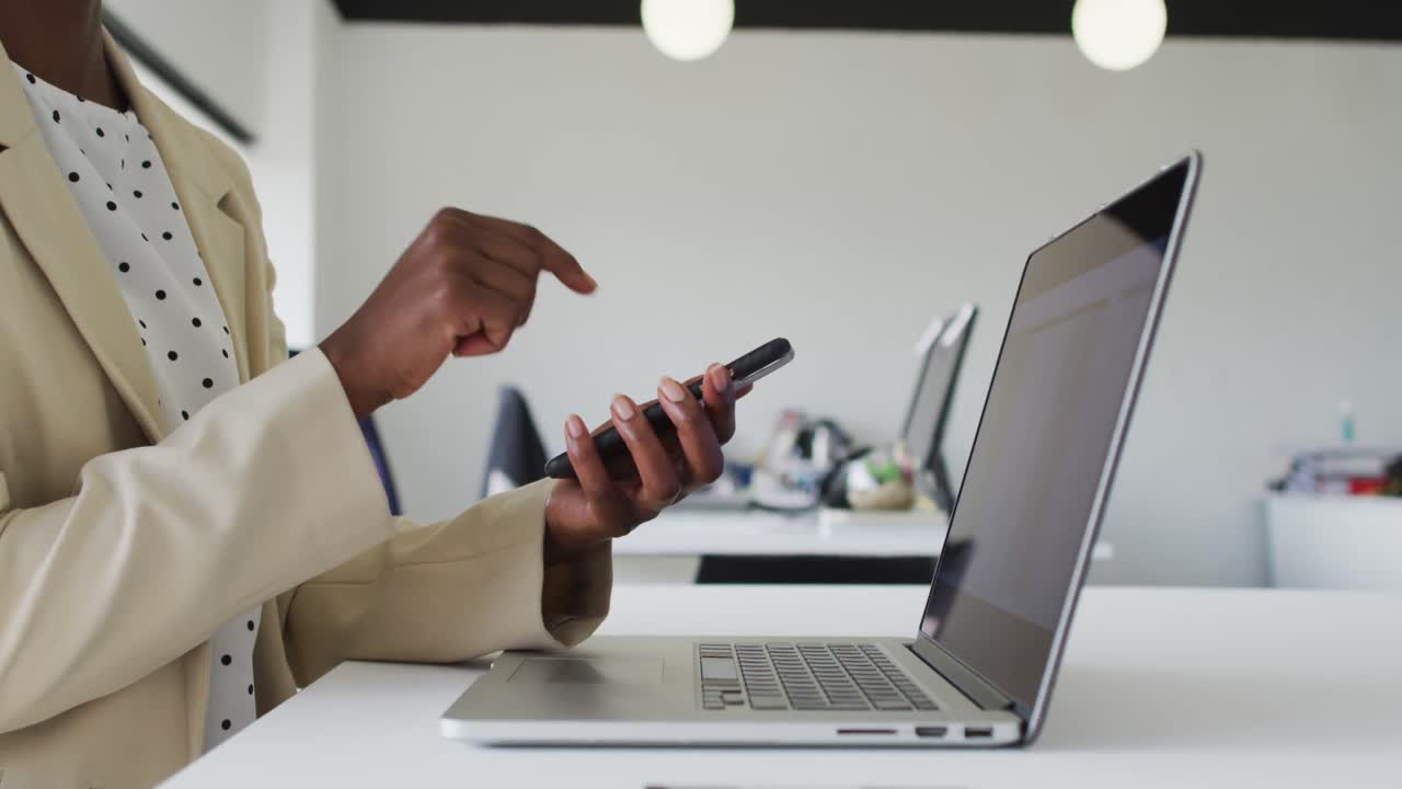 Close-up van de handen van een Afro-Amerikaanse zakenvrouw die aan een bureau zit en een smartphone gebruikt.