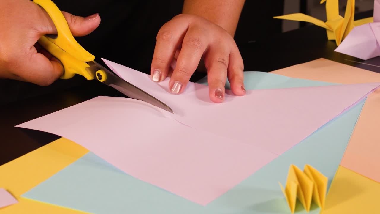 Primo piano di mani che tagliano carta rosa con forbici gialle su un’area di lavoro colorata