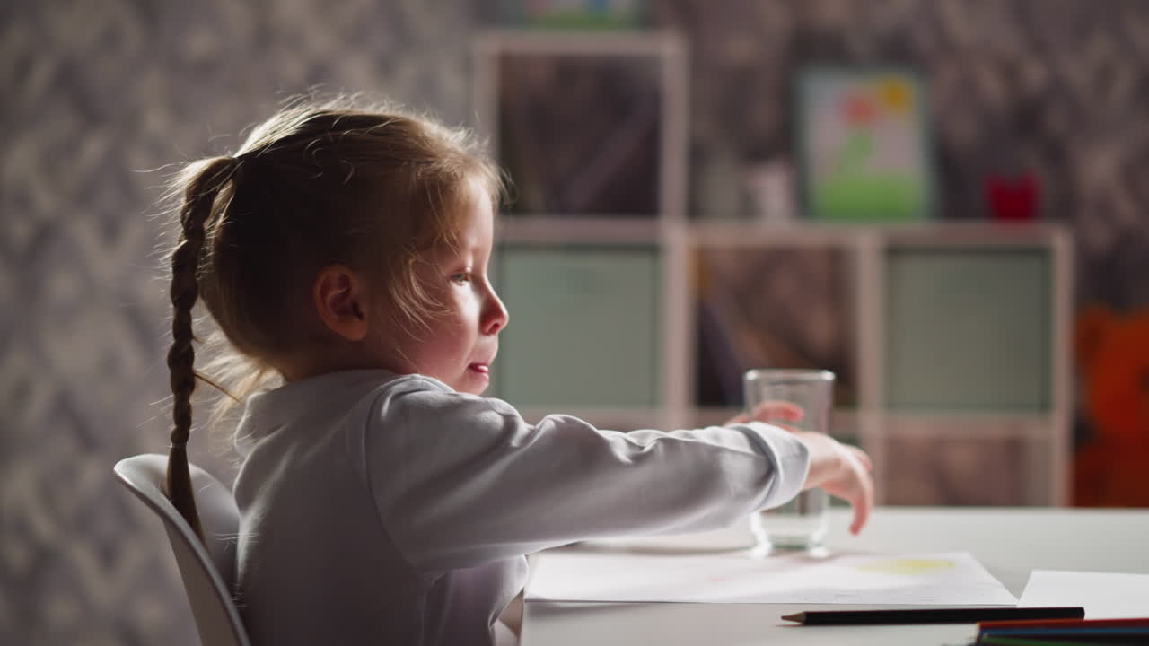 Una bambina in età prescolare con la treccia mette via il bicchiere e inizia a disegnare.