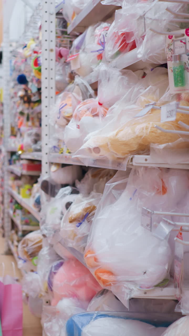 검은 티셔츠와 청바지를 입은 여성이 장난감 가게에서 장난감과 액세서리를 검색하면서, 그녀는 다채로운 선반이 플러시 장난감, 게임 및 장난감으로 가득 차있는 동안 물건에 도달합니다.