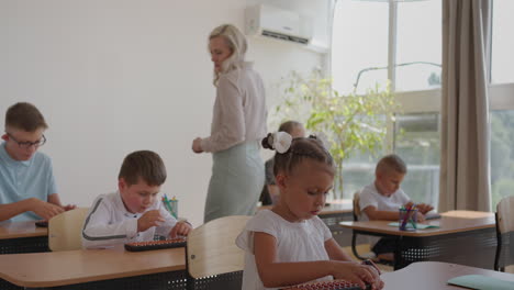 In-Elementary-School-Class:-Enthusiastic-Teacher-walks-between-Rows-of-Bright-Diverse-Children-Explains-Lesson.-Group-of-Smart-Multiethnic-Kids-Learning-New-Stuff.-Side-View-Tracking-Shot