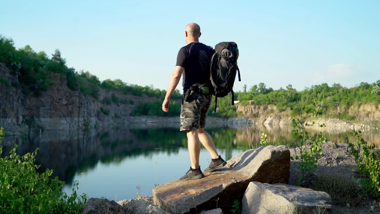 Traveler in sportswear and with a backpack walks along the quarry above the lake and views the beautiful landscape of the locality.