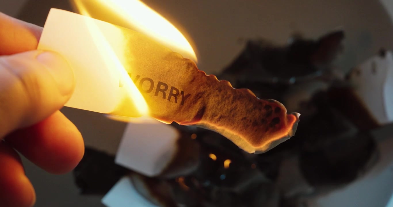 Nahaufnahme eines Zettels mit dem Wort „Sorge“, das in einer Flamme brennt, symbolisiert Stressabbau, Angst, Furcht, Loslassen und emotionale Befreiung.