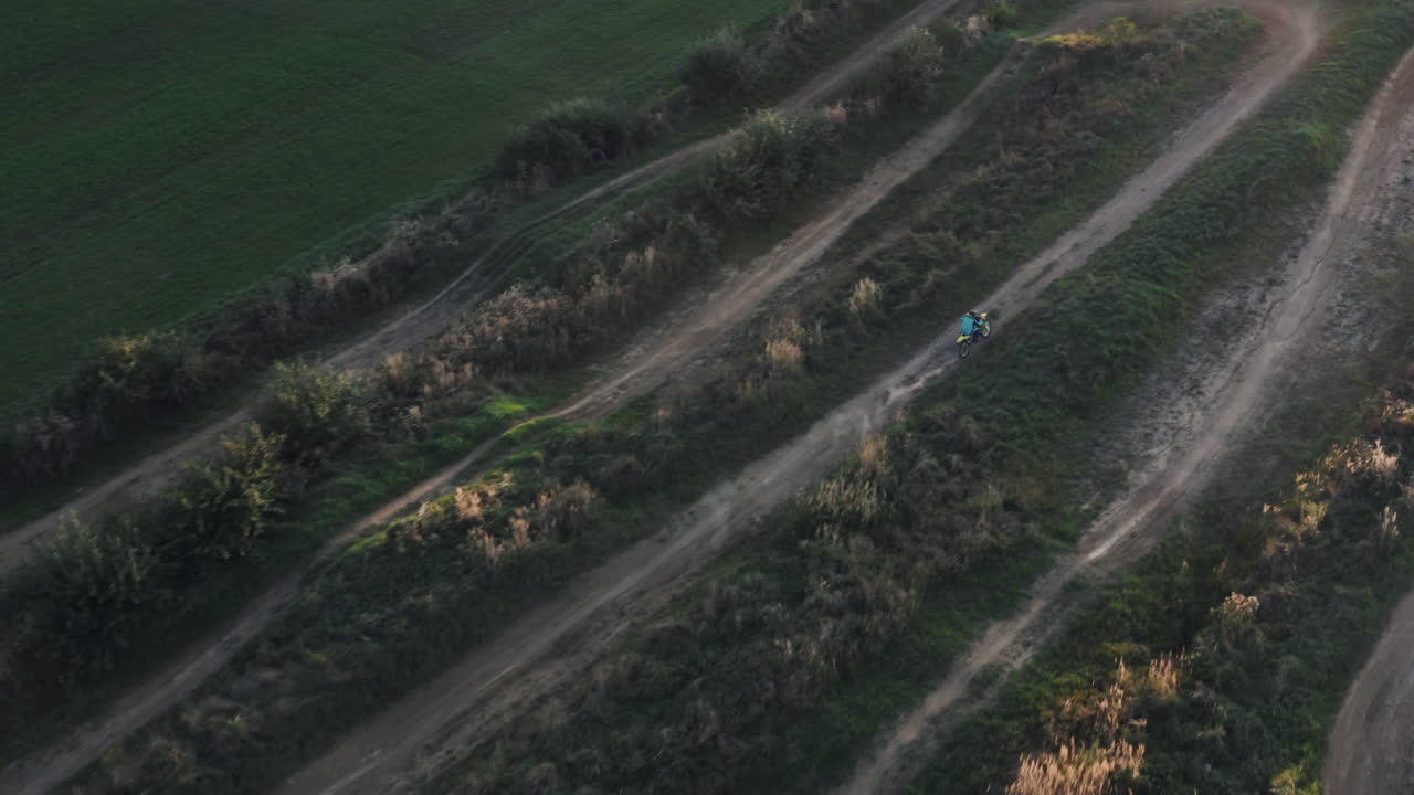 오토바이를 타는 모터사이클의 캠을 따라 가라앉은 자연 풍경을 가로질러 휘어지는 길을 따라, 늦은 오후에 초록색으로 둘러싸여, 위에서 긴 그림자.