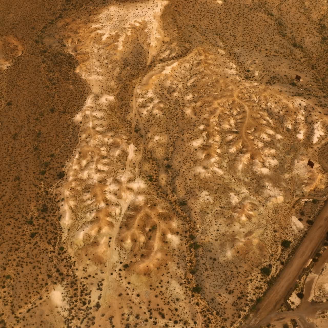 Descending above the driest landscape covered with little plants. Top view over the California desert near the parking lot and highway