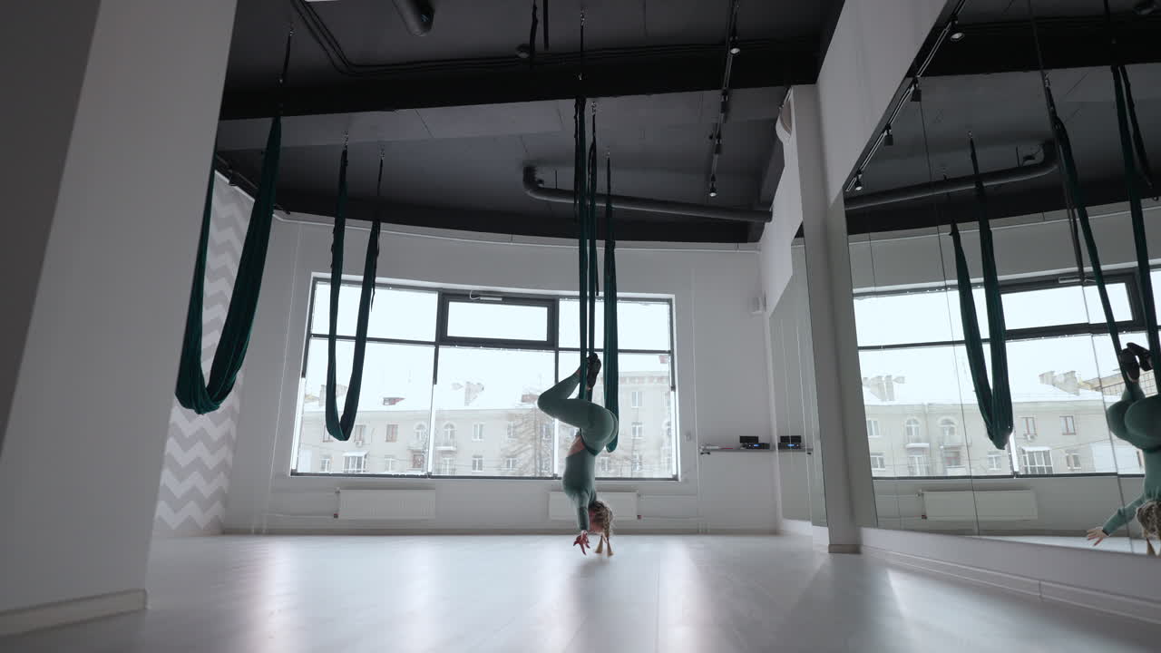 Attraente istruttrice di fitness esegue esercizi di yoga aereo antigravità in un'amaca verde. Una giovane donna flessibile si esercita con un'altalena per aero stretching in un centro fitness. Concetto di routine di yoga fitness femminile.