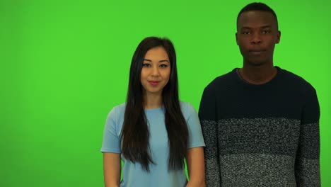 a young asian woman and a young black man talk to the camera - green screen studio