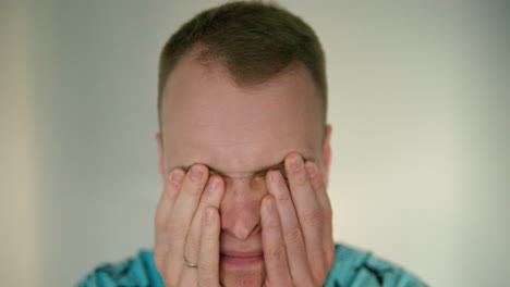 close up of man's sad face covering and rubbing his eyes