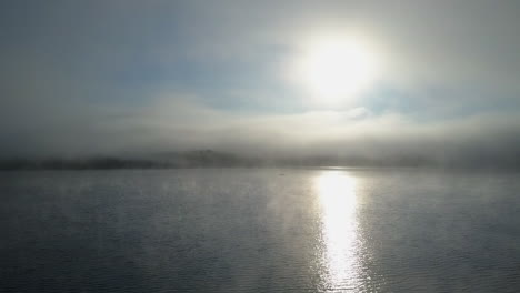 beautiful sunrise aerial over foggy lake with sun beam and one boat