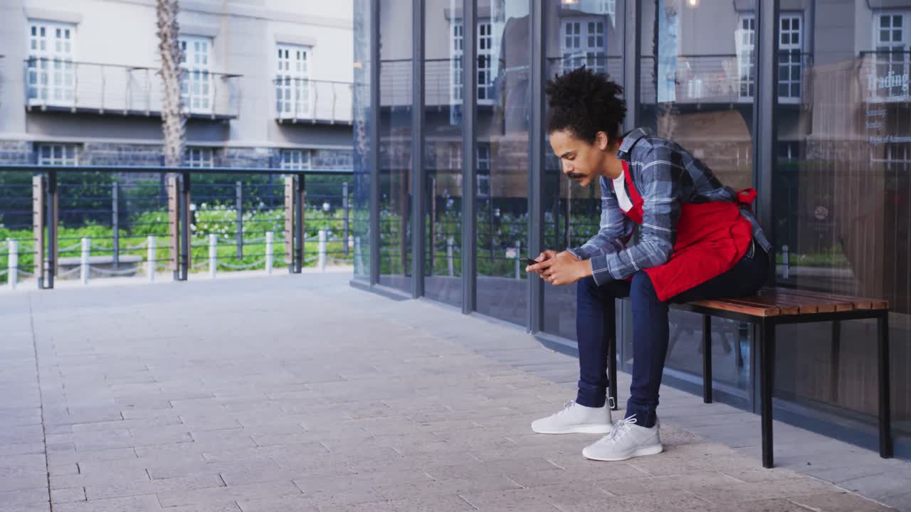 barista de raza mixta con bigote que lleva un delantal hablando en un teléfono inteligente