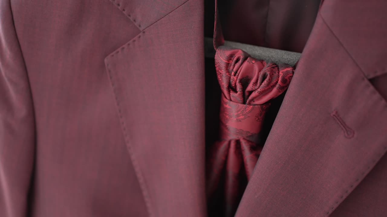 Detailed close up of a burgundy wedding suit with a matching cravat tie