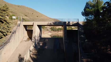 Drohnenflug-über-Einen-Der-Überlaufkanäle-Des-Stausees-Güéjar-Canales-In-Spanien-Durch-Die-Öffnung-Und-Mit-Blick-Auf-Einen-Wasserturm