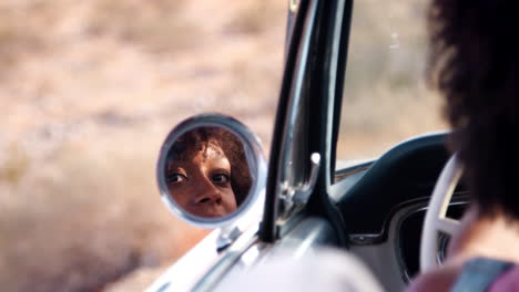 Young-black-woman-in-open-top-car-reflected-in-wing-mirror