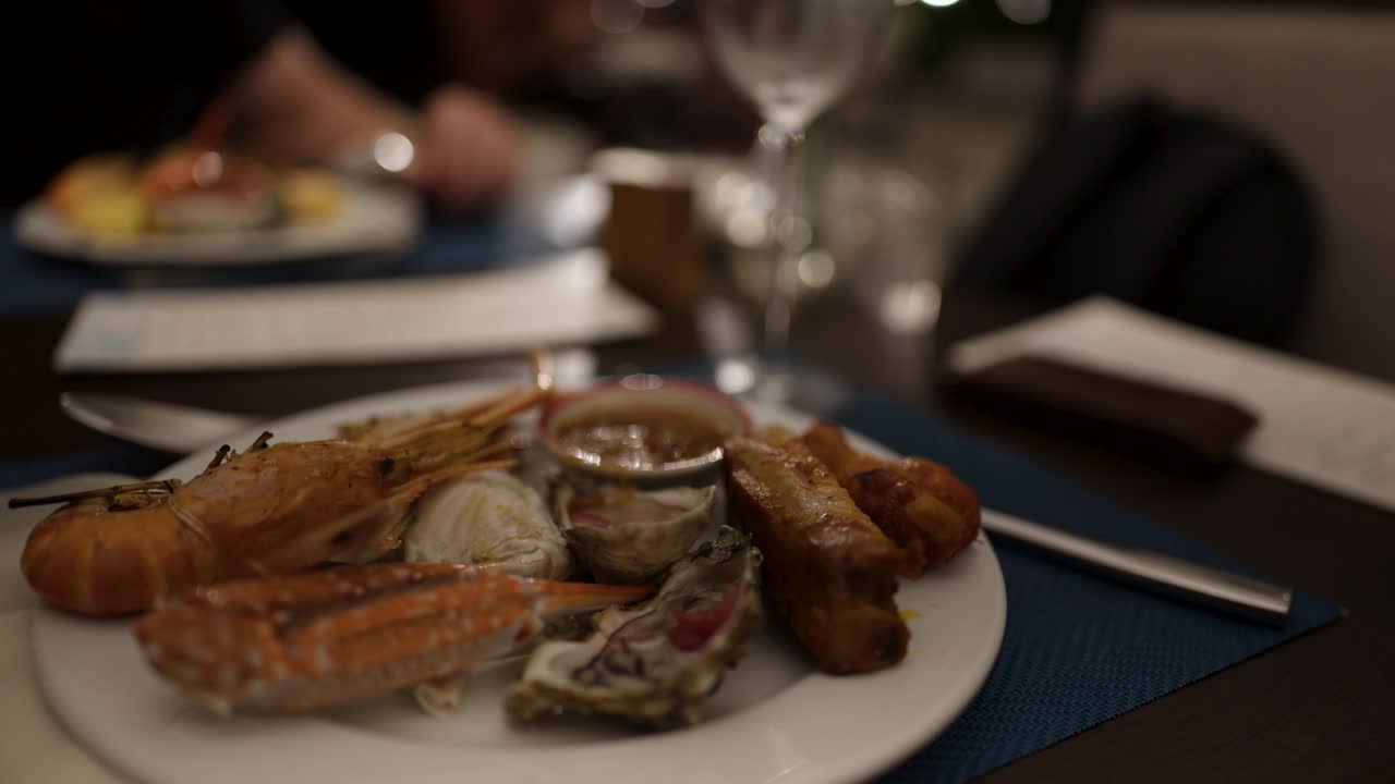 Plate of shrimp, oyster, crab, and sauce on restaurant table, soft evening lighting, shallow focus