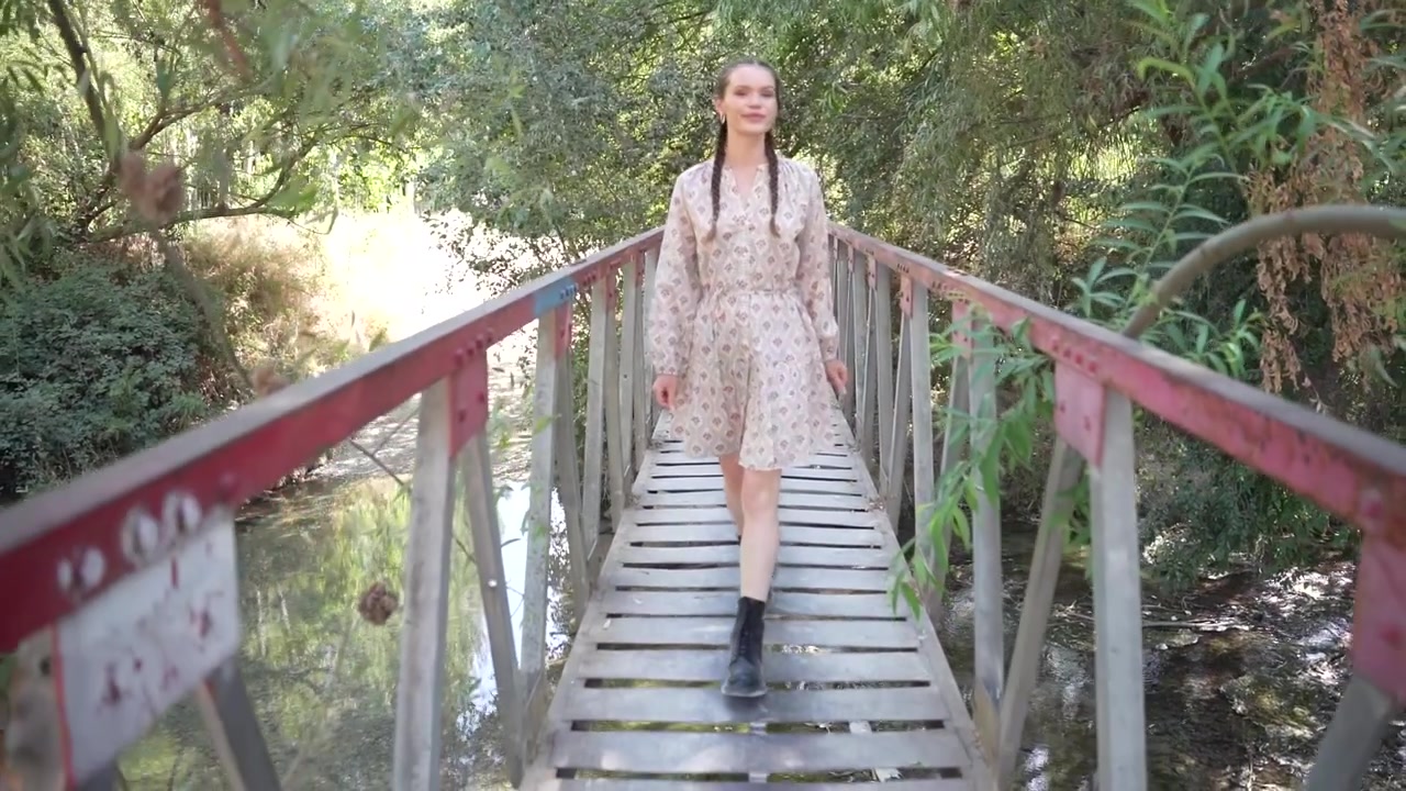 Una donna cammina con grazia lungo un ponte di legno splendidamente costruito, circondata da una vegetazione lussureggiante.