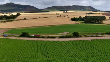 aerial view of a truck traveling on a country road through lush farmland and rolling hills under overcast daylight in kinross, scotland. smooth lateral camera movement