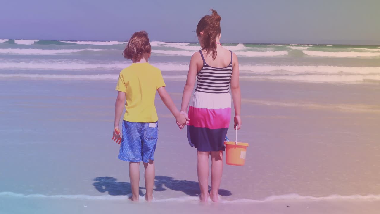 Fratello e sorella caucasici di spalle in piedi sulla spiaggia.