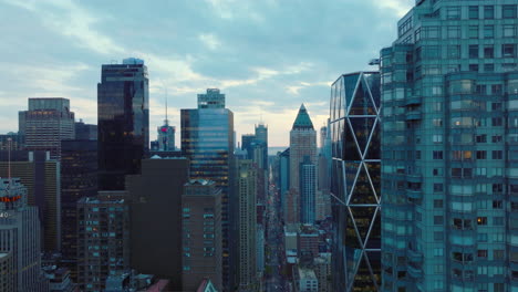 Forwards-fly-along-row-of-modern-tall-buildings.-Upper-storeys-of-skyscrapers-high-above-streets.-View-against-sky-at-twilight.-Manhattan,-New-York-City,-USA