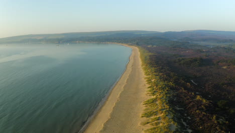una toma aérea volando a lo largo de la playa británica de arena de la bahía de studland en la costa de dorset al amanecer con una hermosa luz en el verano