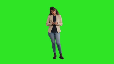 retrato de estudio de longitud completa de una maestra o mujer de negocios de pie contra una pantalla verde usando un teléfono móvil para enviar mensajes o navegar en línea 1