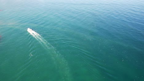 Velero-Rodea-El-Muelle-Rocoso-Con-Aguas-Azules,-Pájaros-Marinos-Volando-Sobre-El-Vehículo