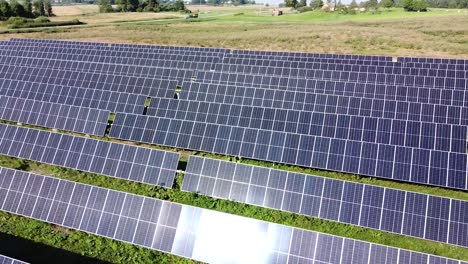 Sun-reflects-on-solar-panel-cells-in-agricultural-landscape,-aerial-drone-view