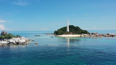 aerial drone of kepayang island in belitung indonesia with a large white lighthouse surrounded by forest on a tropical sunny day