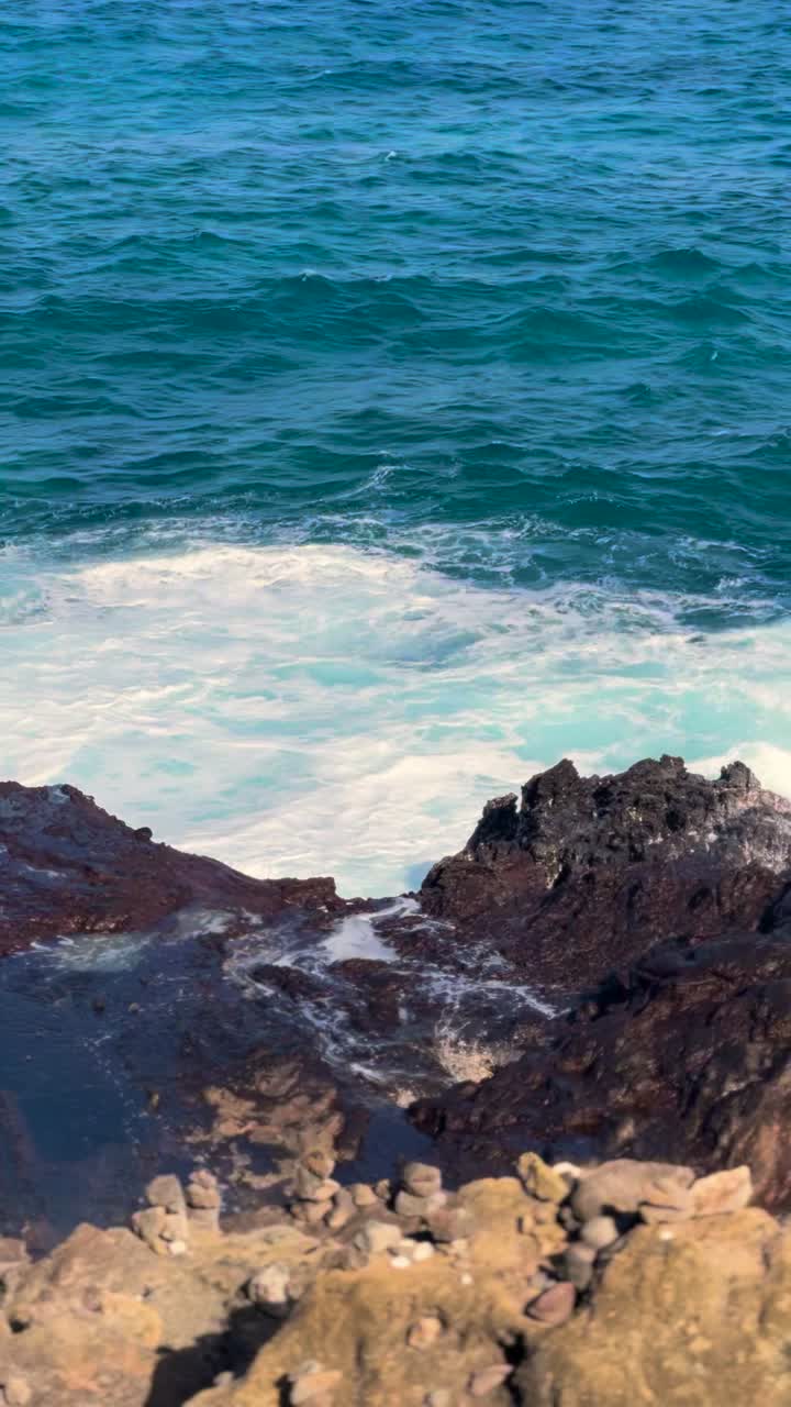 Waves crash at Halona Blowhole in Oahu, blue ocean, rocky coast