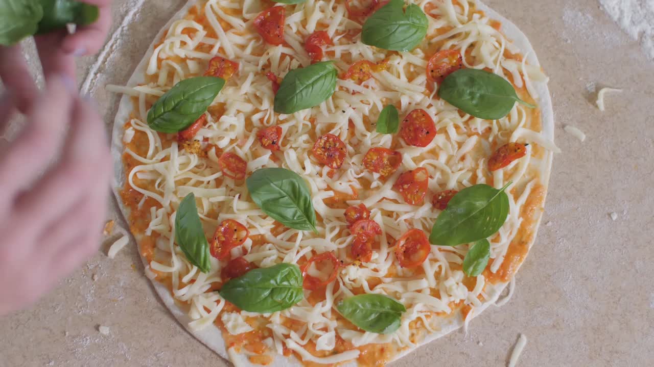 A hand putting fresh basil on a homemade pizza from above