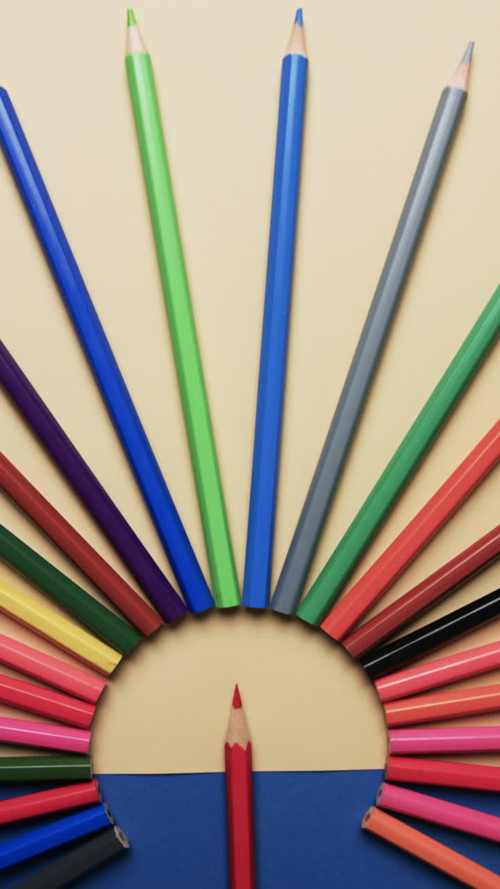 Vertical video of overhead view of crayons arranged on beige and blue background, in slow motion